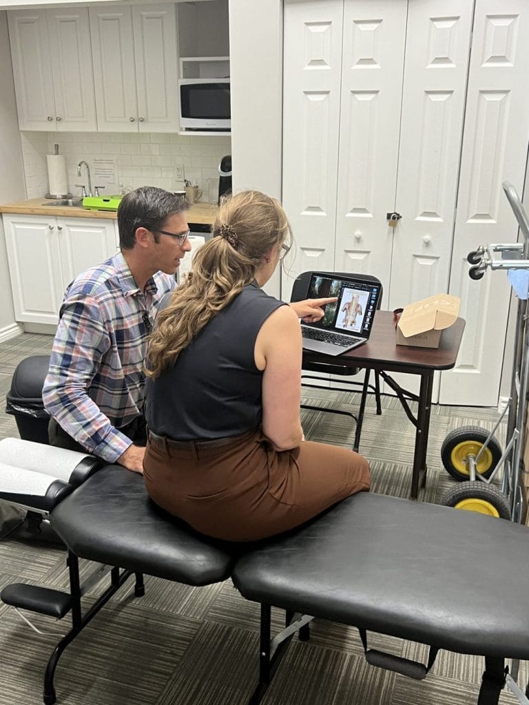 Dr. Nik Dukovac reviewing spinal anatomy on a laptop with an employee after a screening